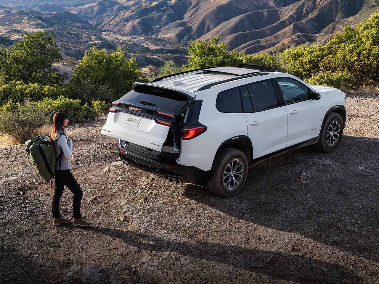A Woman with a Hiking Backpack on, Walking up to a GMC Vehicle with the Trunk Opening.