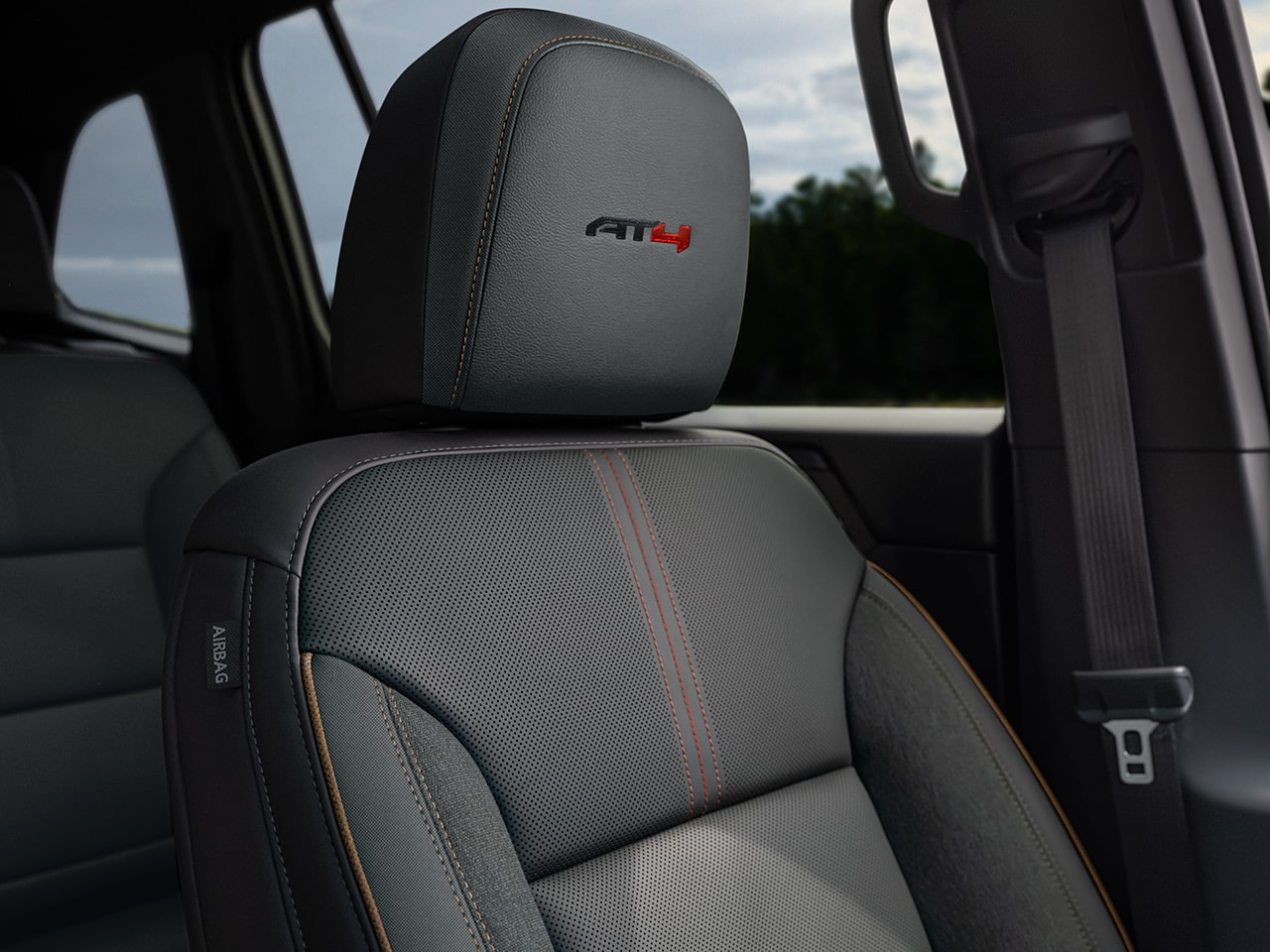 An Interior Shot of a GMC AT4 Vehicle’s Perforated Gray Leather Seat with Orange Stitching and an AT4 Logo