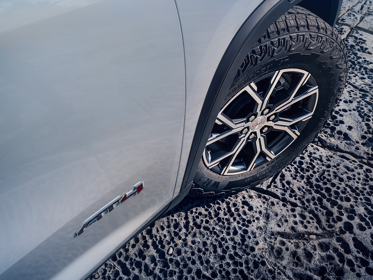 A Close-up of a White GMC AT4 Vehicle’s Front Wheel and AT4 Badging on a Bumpy Surface