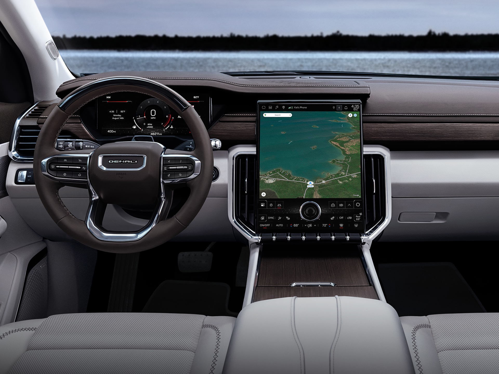The Interior of a GMC Denali Vehicle Showing the Dashboard, Steering Wheel with the Denali Logo, and a Large Central Display Screen with a Map, along with Light Gray Seats