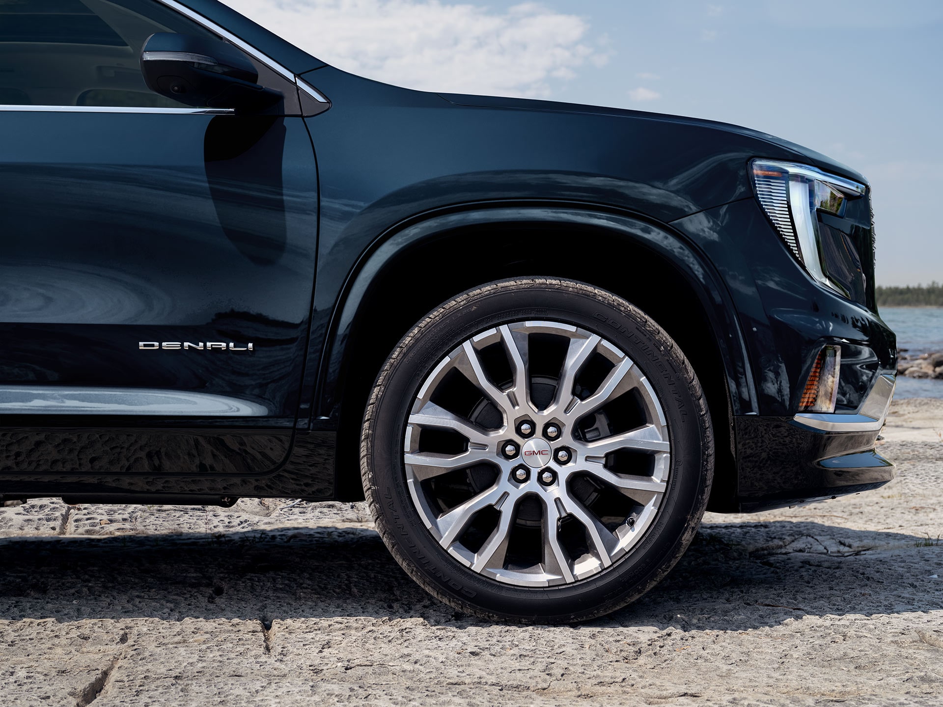 A Close-up of the Front Wheel and Dark Blue Side of a GMC Denali SUV with the Denali Badge Visible