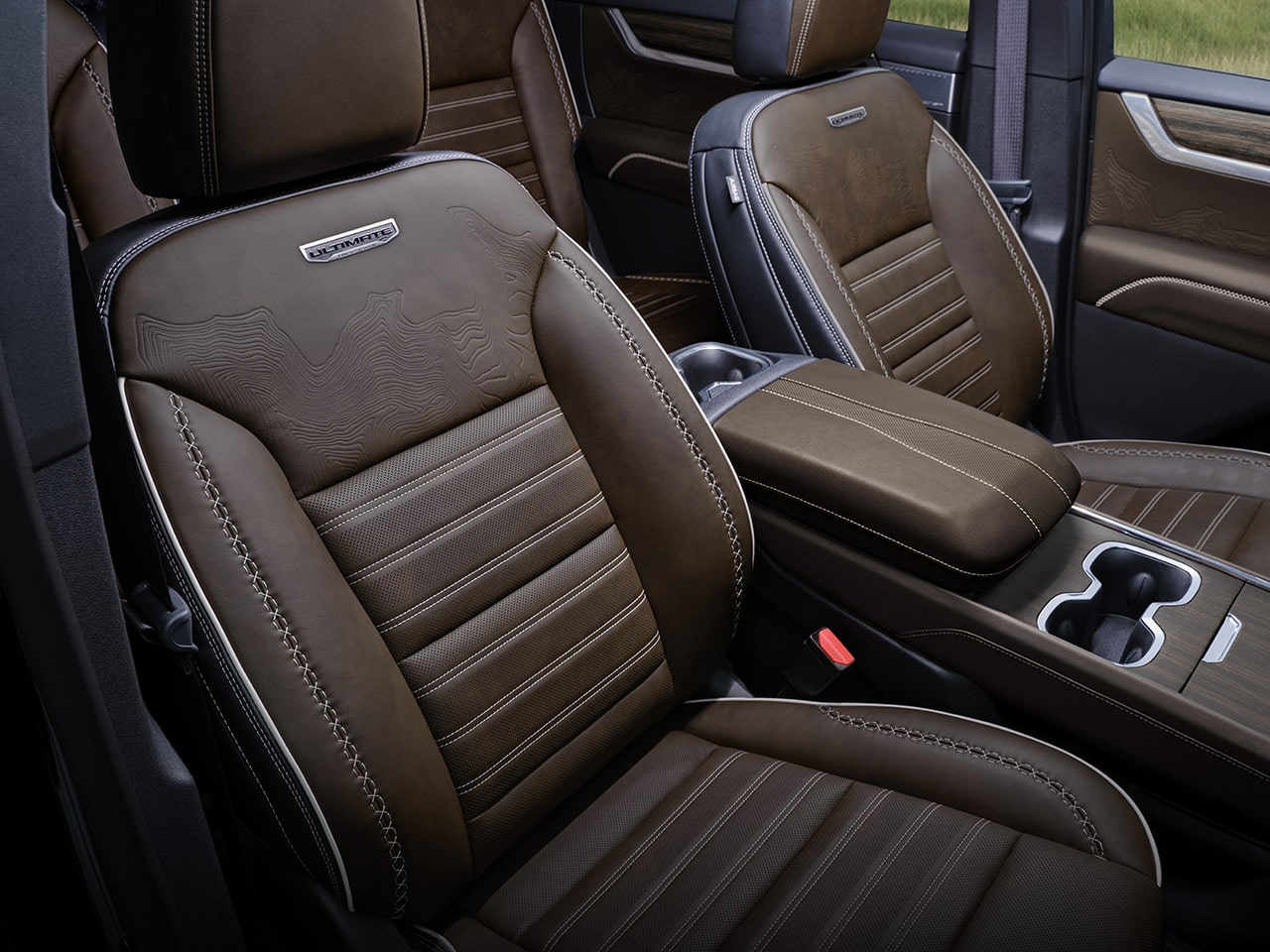 A Close-up of the Brown Leather Seats with White Stitching and the Ultimate Emblem in a GMC Vehicle Interior