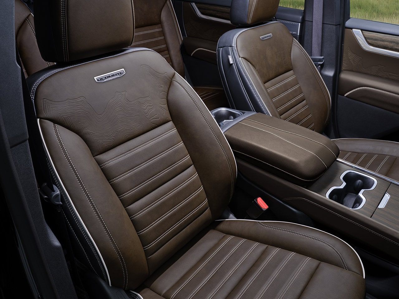 A Close-up of the Brown Leather Seats with White Stitching and the Ultimate Emblem in a GMC Vehicle Interior