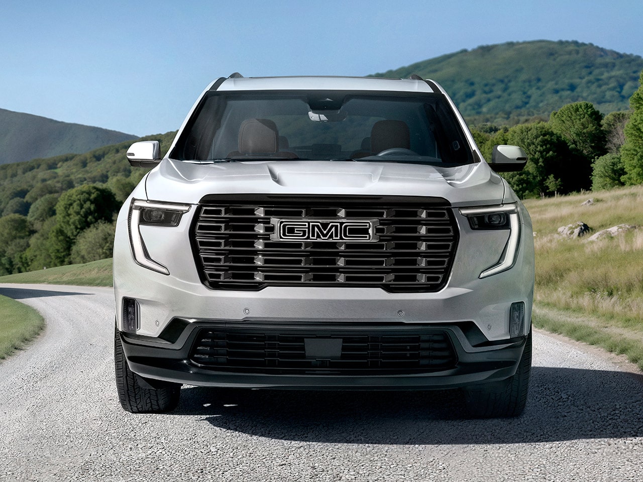 Front View of a White GMC SUV With the GMC Logo on the Grille Against a Backdrop of Green Rolling Hills