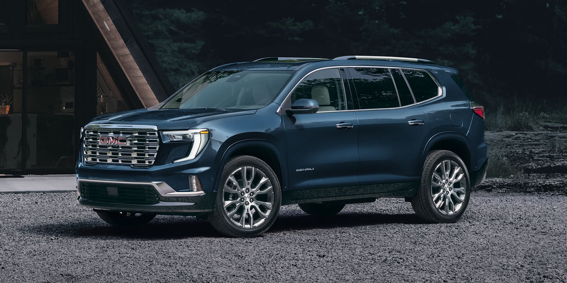 A Dark Blue GMC Denali SUV Parked on a Gravel Surface in Front of a Modern House at Dusk