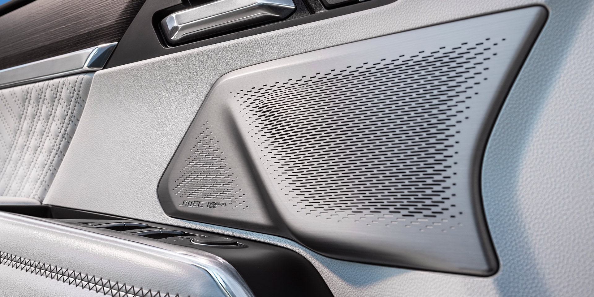 The Interior Door Panel of a GMC Vehicle with a Silver Bose Speaker Grille and White Leather with Intricate Stitching