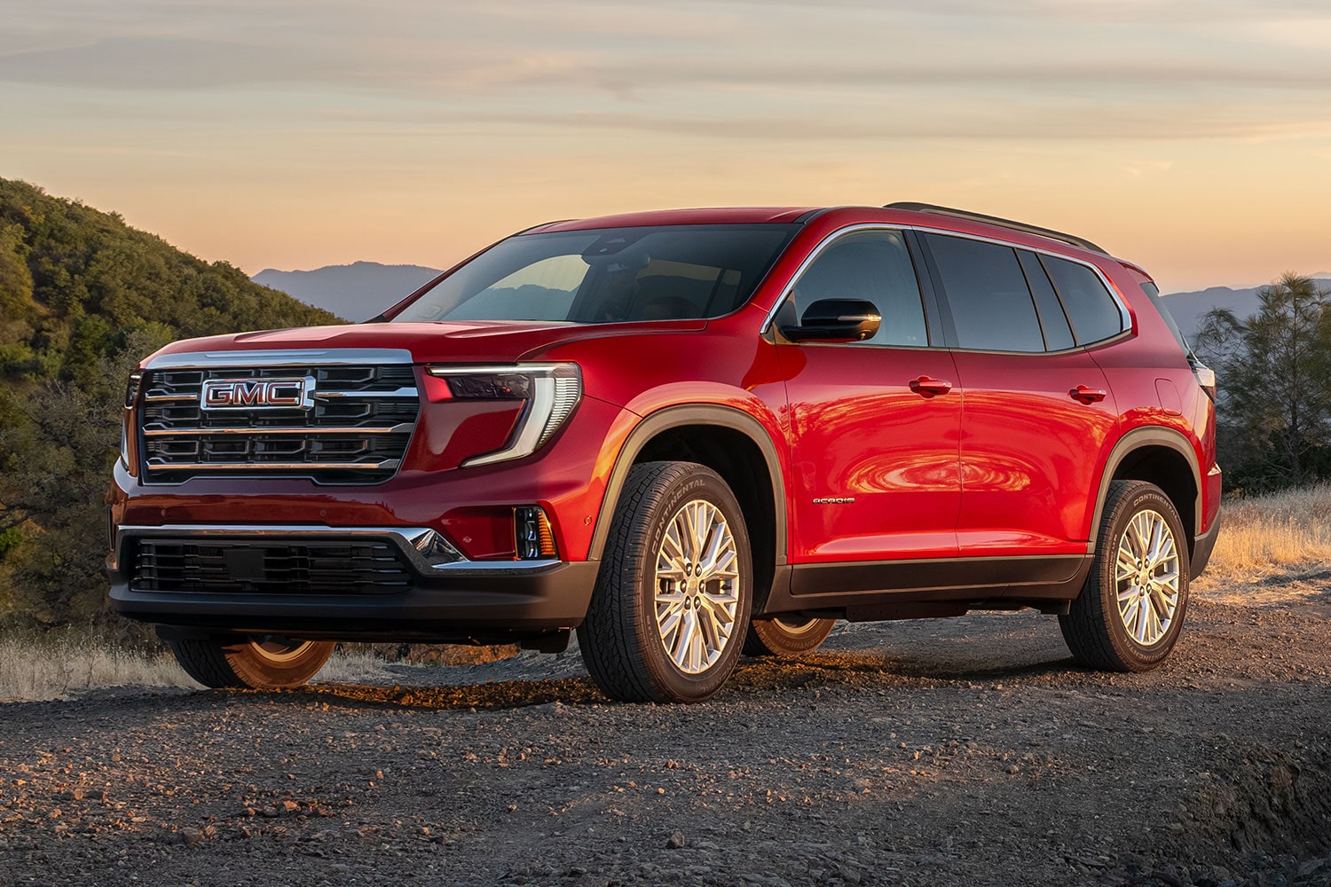 Red GMC SUV Parked On a Dirt Road At Sunset In a Hilly Landscape Under an Orange Sky