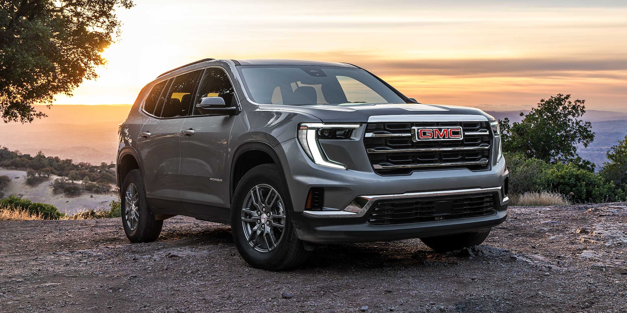 A Gray GMC SUV Parked on a Dirt Road with a Sunset Backdrop and Mountains in the Distance