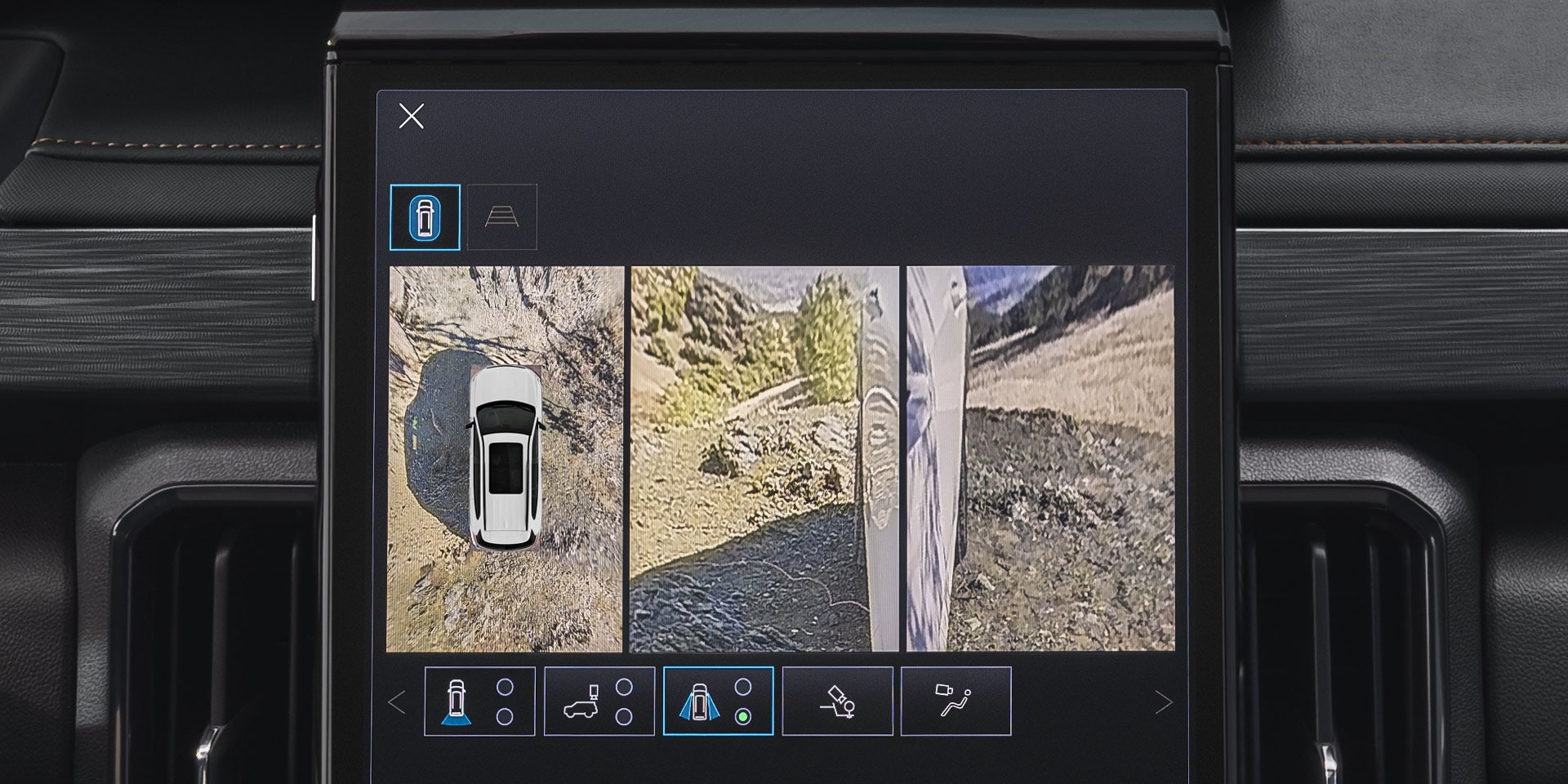 A Close-Up Of a GMC Vehicle's Infotainment Screen Showing a Split View Of a White Vehicle From Above and a Side Camera View Of an Unpaved Road