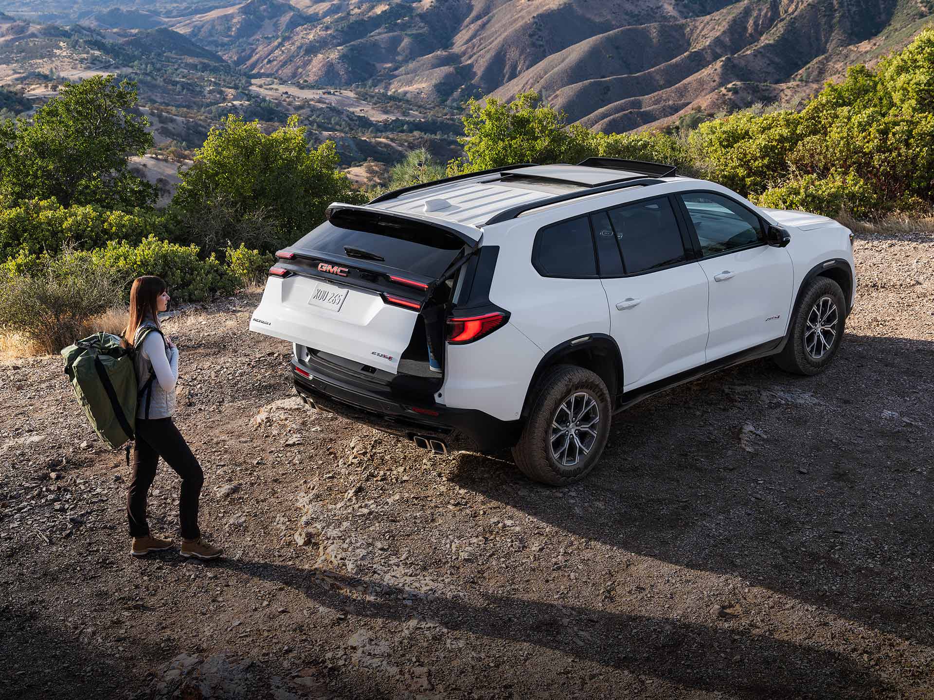 A Woman with a Hiking Backpack on, Walking up to a GMC Vehicle with the Trunk Opening.
