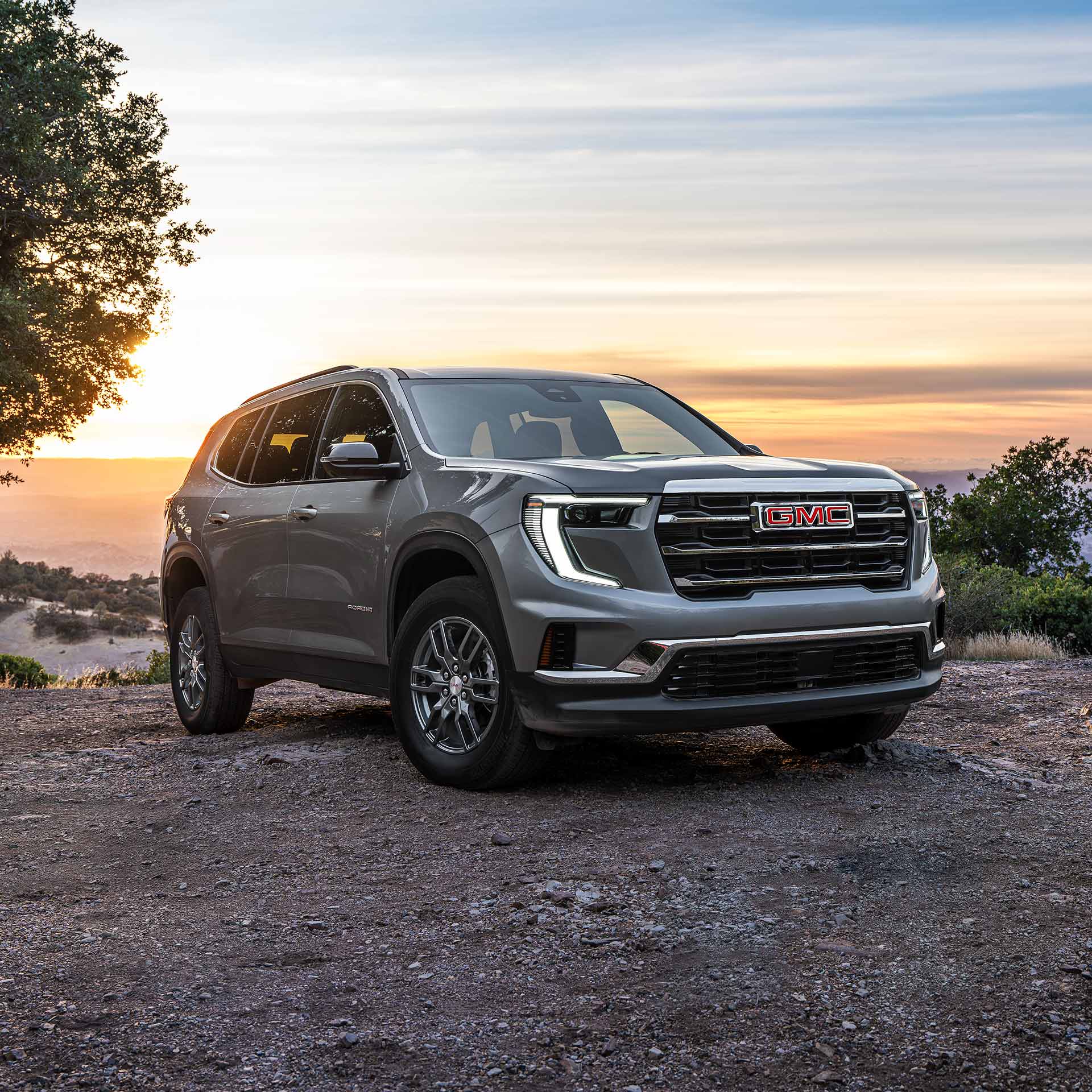 A Gray GMC SUV Parked on a Dirt Road with a Red GMC Logo on the Grille at Sunset