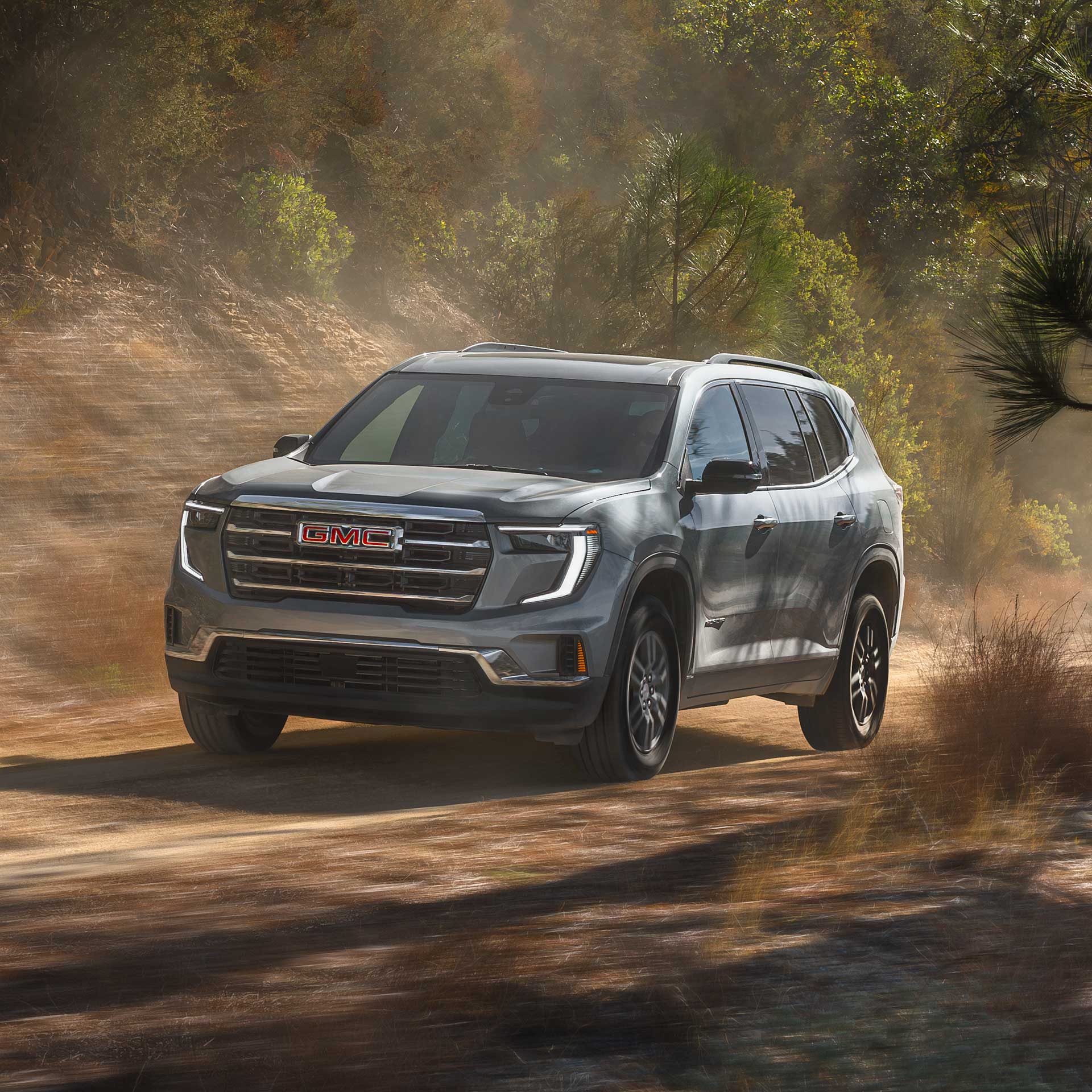 A Gray GMC SUV Driving on a Dirt Road with Green Trees in the Background