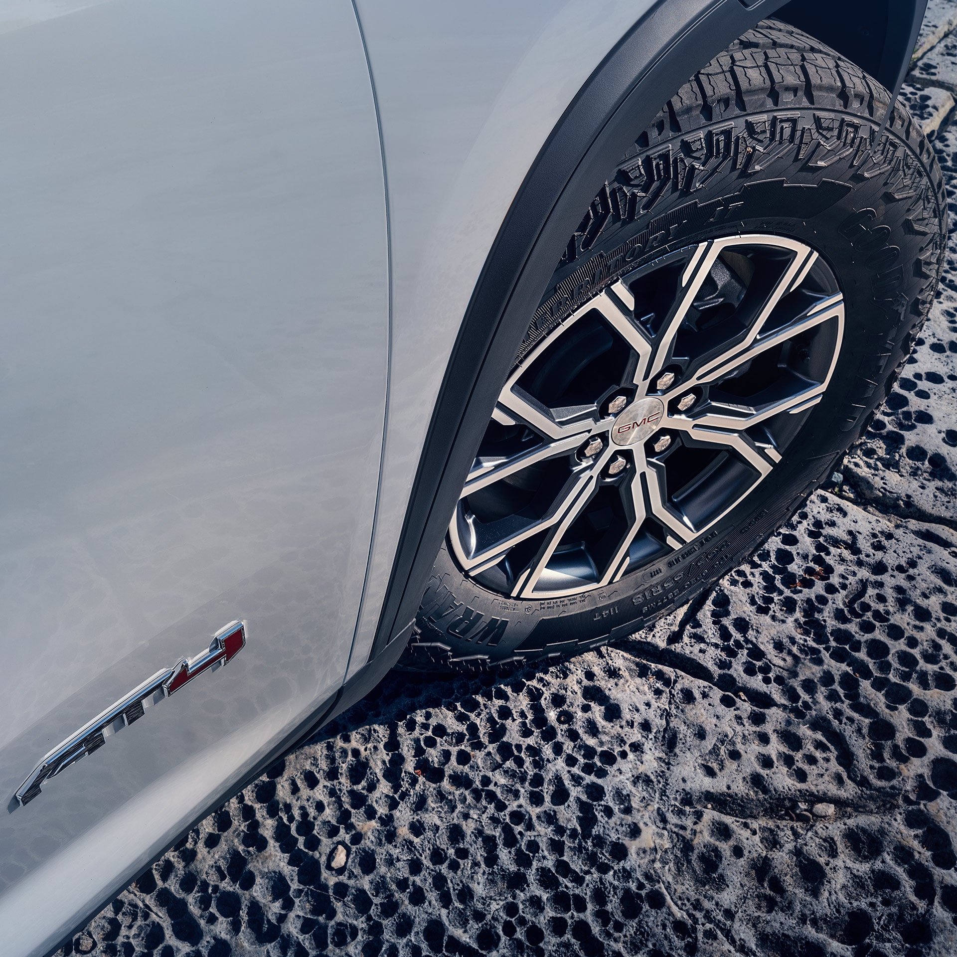 A Close-up View of a Light Gray GMC AT4 Vehicle's Wheel and Tire on Rocky Terrain