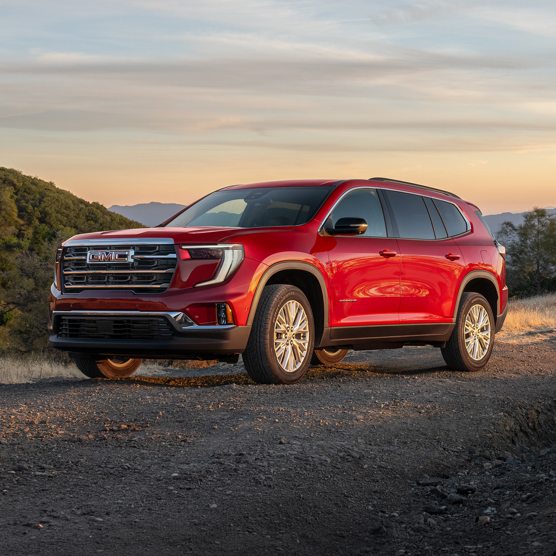 Red GMC SUV Parked on a Dirt Road At Sunset In a Hilly Landscape Under an Orange Sky