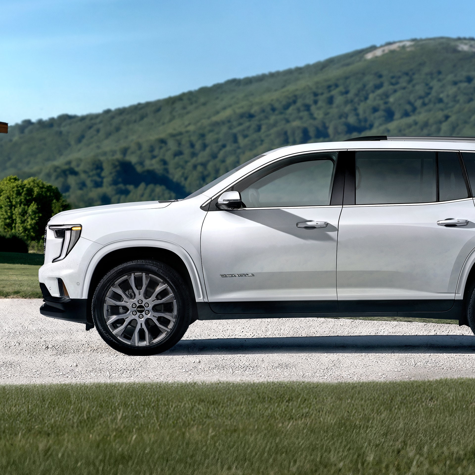 A White GMC Denali SUV Parked on a Gravel Road with Green Mountains in the Background