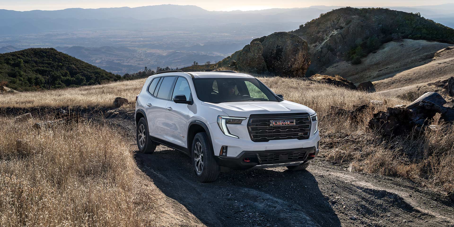 A White GMC SUV Positioned on a Dirt Trail in a Dry Hilly Landscape with Mountains in the Background