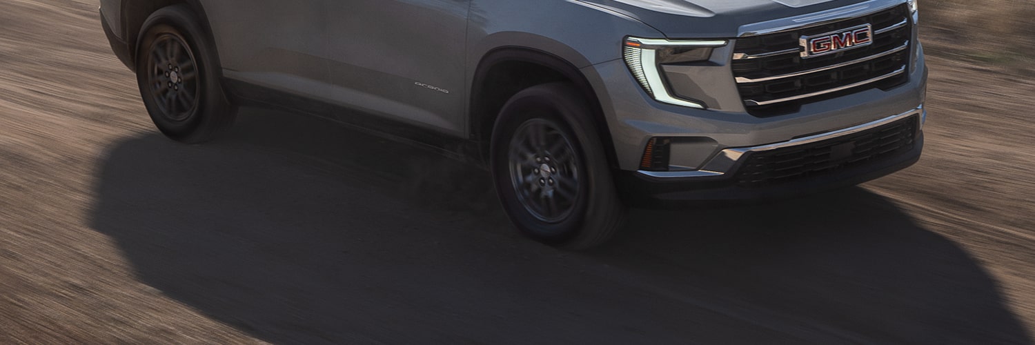 Gray GMC SUV Driving on a Winding Dirt Road With Blurred Green Foliage in the Background