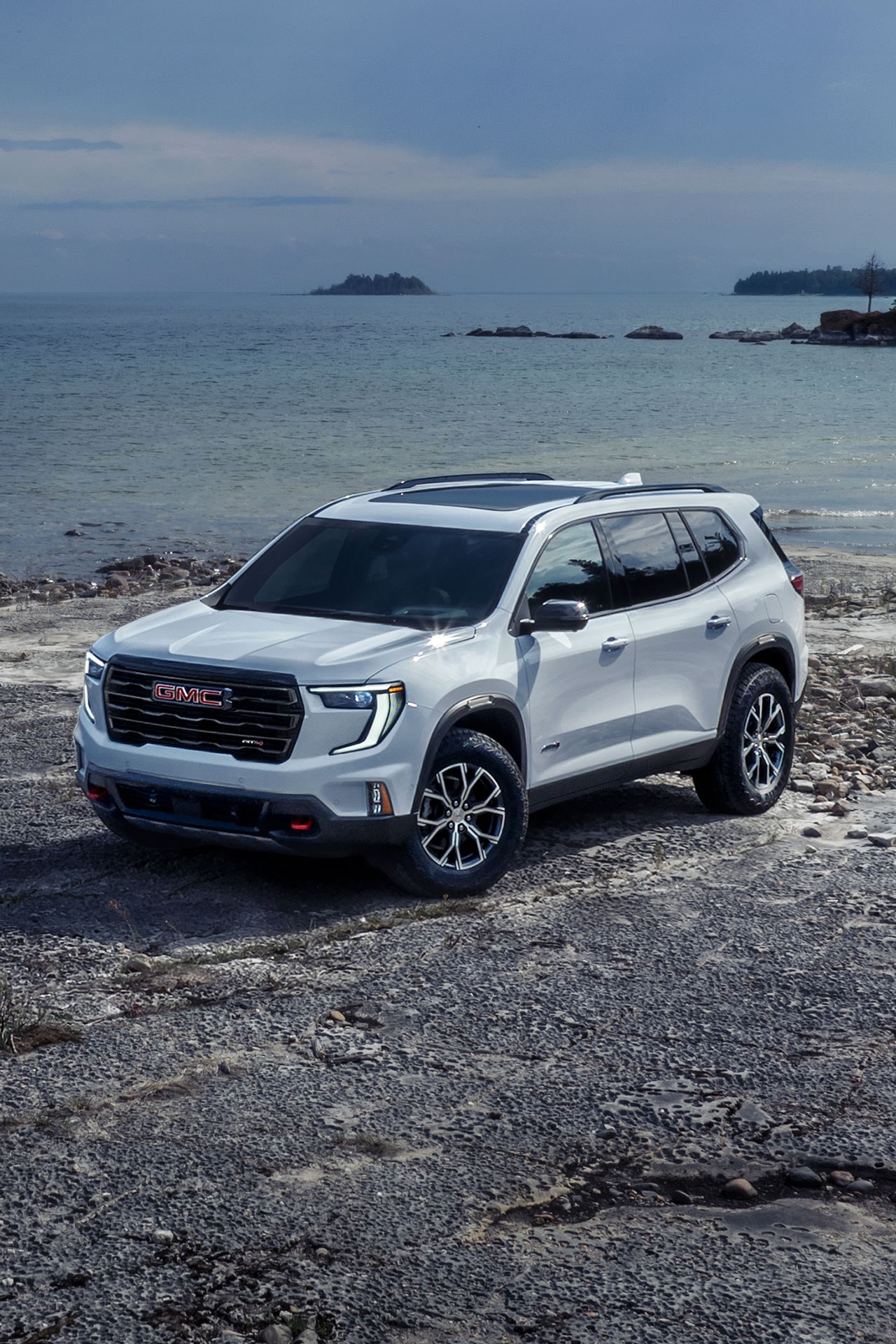 White GMC SUV With the GMC Logo on the Grille Parked on a Rocky Beach Beside the Ocean