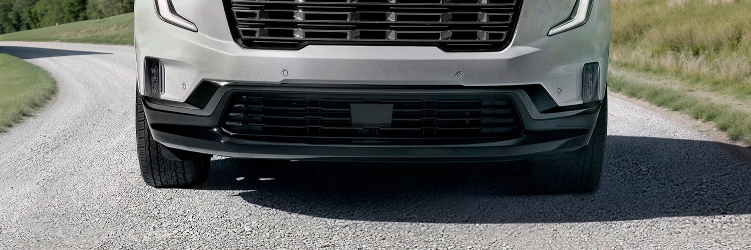 Close-up of the Front Bumper And Lower Grille of a Light-Colored SUV Driving on a Gravel Road