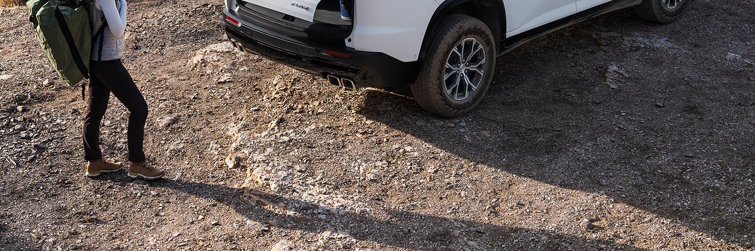 A Woman with a Hiking Backpack on, Walking up to a GMC Vehicle with the Trunk Opening.