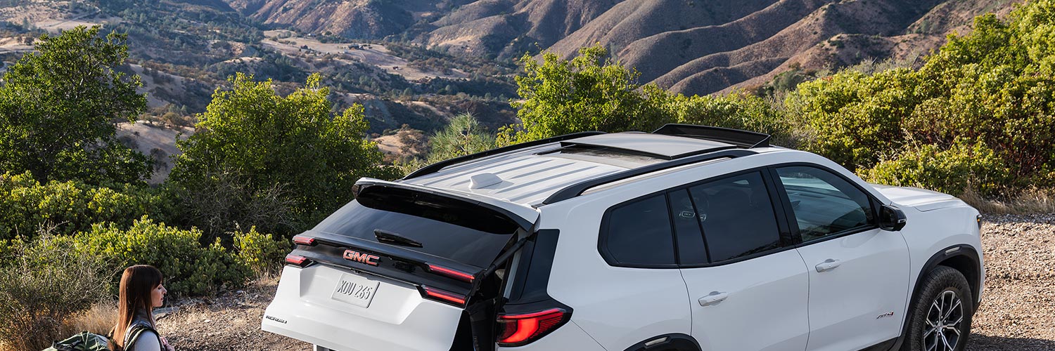 A Woman with a Hiking Backpack on, Walking up to a GMC Vehicle with the Trunk Opening.