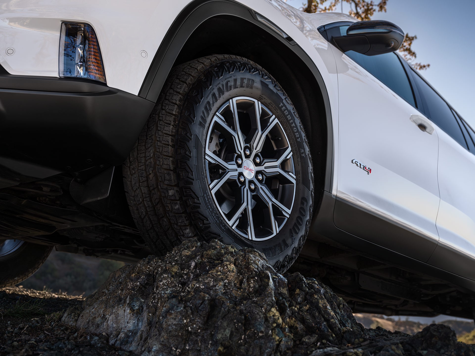 Close-up of a GMC SUV Front Wheel With a Goodyear Wrangler Territory AT Tire Climbing Over Rocks