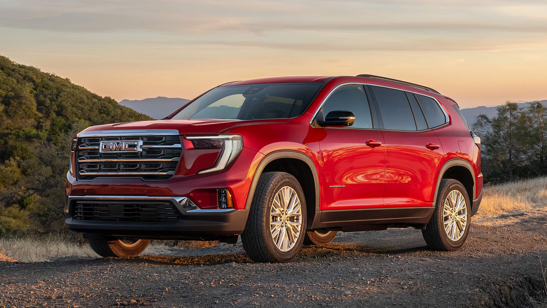 Red GMC SUV Parked on a Dirt Road At Sunset In a Hilly Landscape Under an Orange Sky