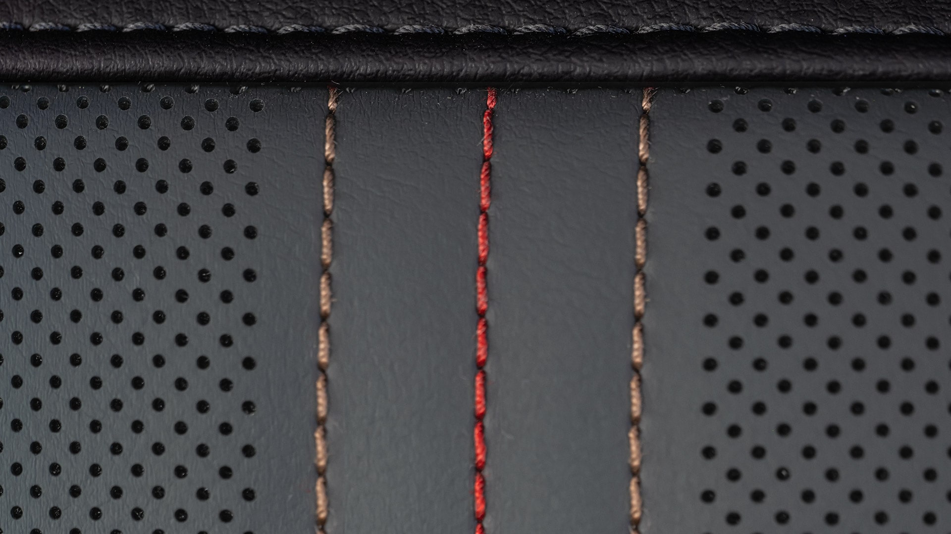A Close-up View of Dark Gray Perforated Leather with Red and Beige Vertical Stitching