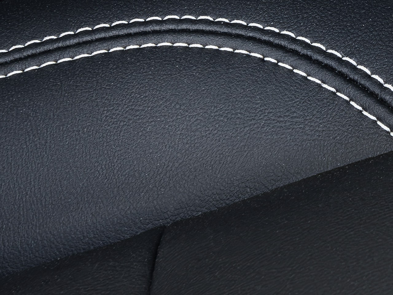 A Close-up View of Dark Gray Material with White Contrast Stitching Forming a Curve