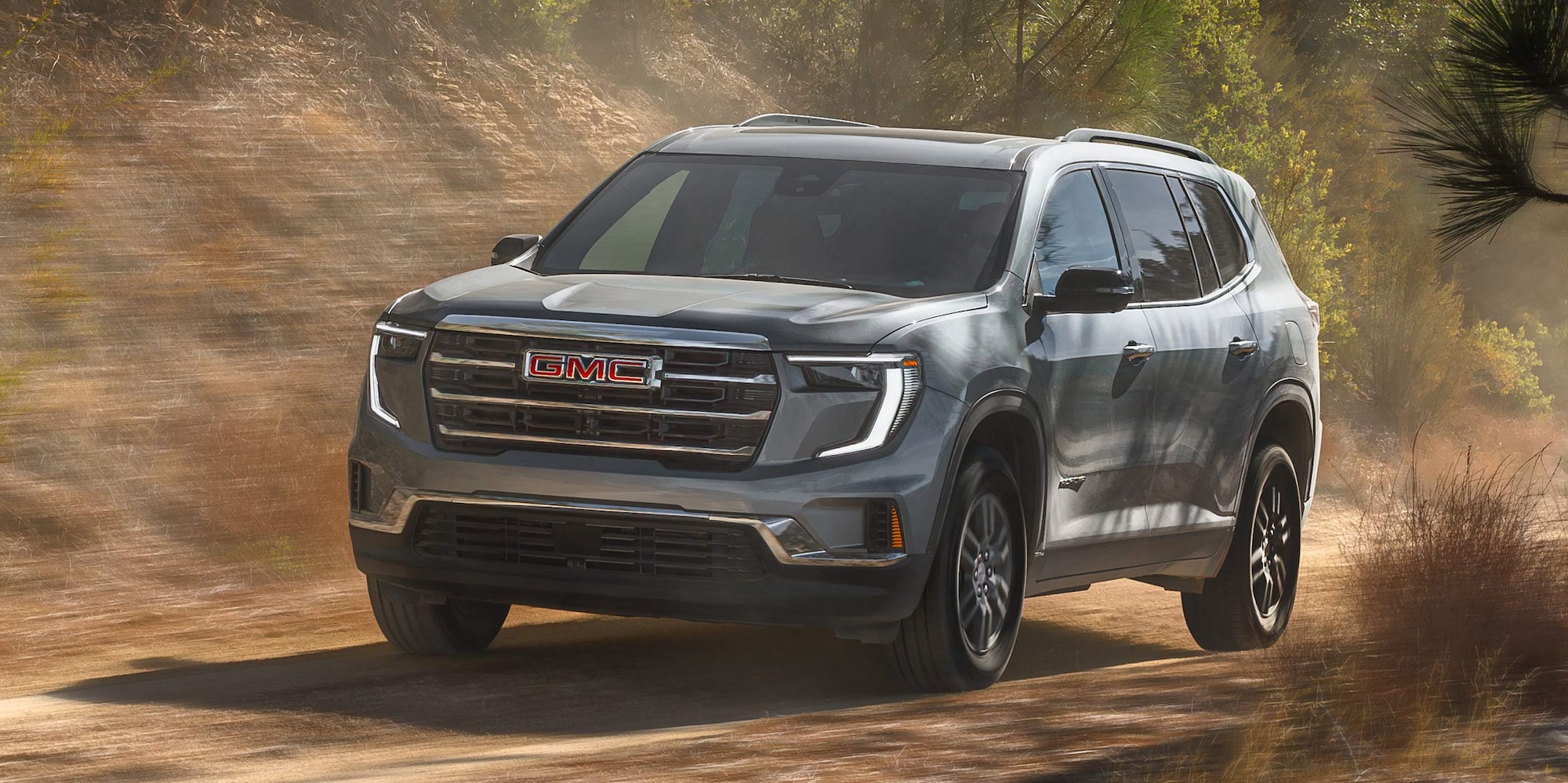A Gray GMC SUV Driving on a Dirt Road with Green Trees in the Background