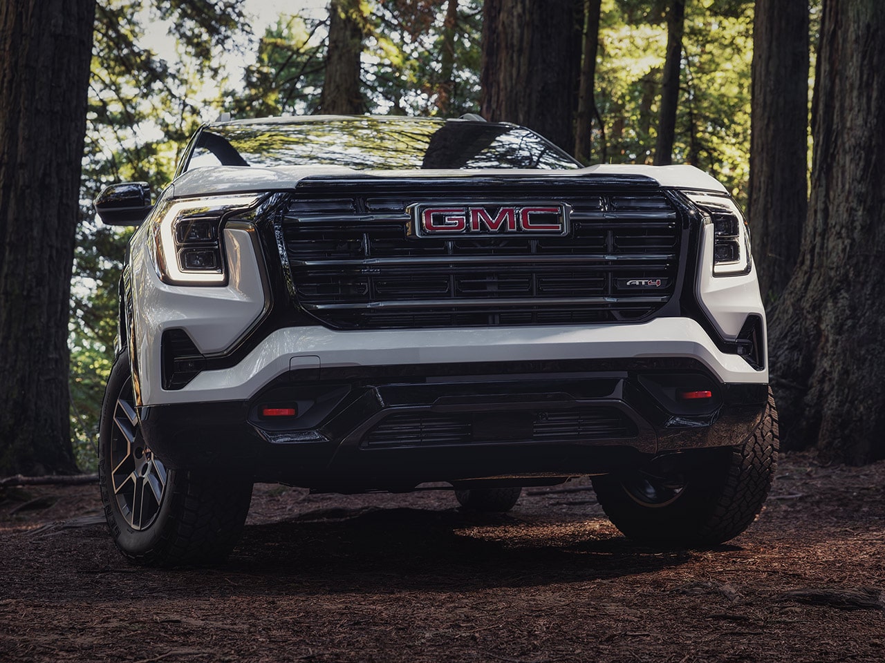 A Front View of a White GMC AT4 SUV with a Distinctive Grille and Bright Headlights Parked on a Forest Trail