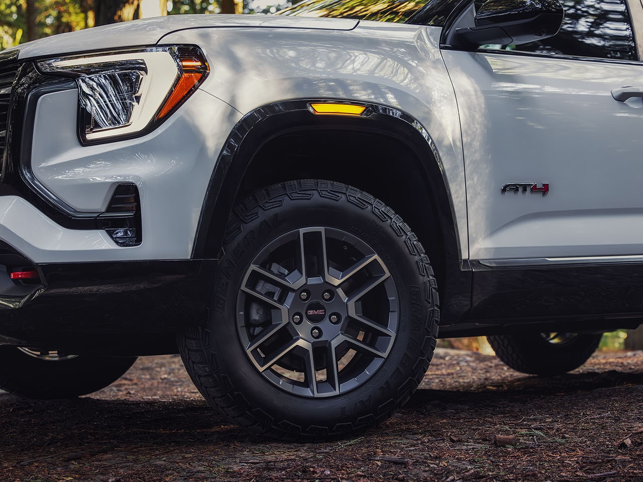 A Close-up of the Front Wheel and Fender of a White GMC AT4 SUV Showing the All-Terrain Tire and GMC Wheel Logo