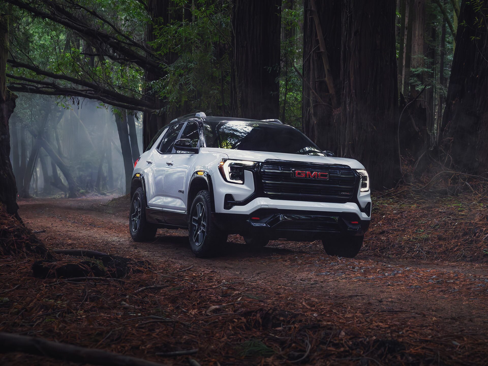 A White GMC SUV is Parked on a Dirt Road in a Dense Forest with Tall Trees