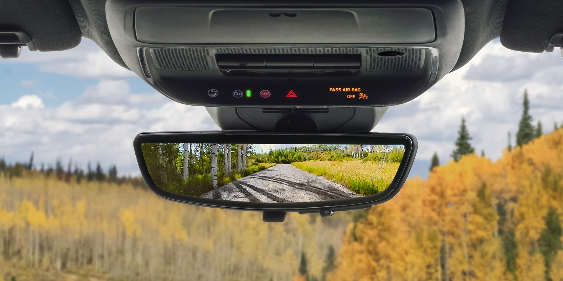 The Rearview Mirror of a GMC Vehicle Reflects a Dirt Road Winding Through Autumnal Yellow and Green Trees