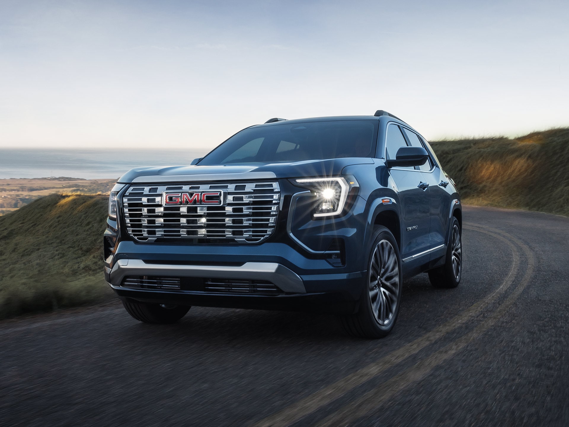 A Dark Blue GMC Denali SUV Driving on a Winding Road Overlooking a Scenic Coastal Landscape