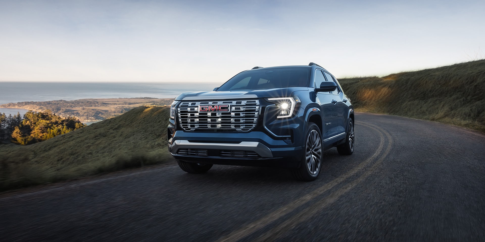 A Dark Blue GMC Denali SUV Driving on a Winding Road Overlooking a Scenic Coastal Landscape