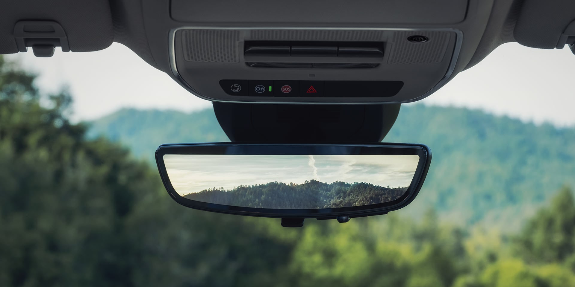 An Interior View of a GMC Vehicle with the Rearview Mirror Reflecting a Green Mountain Landscape
