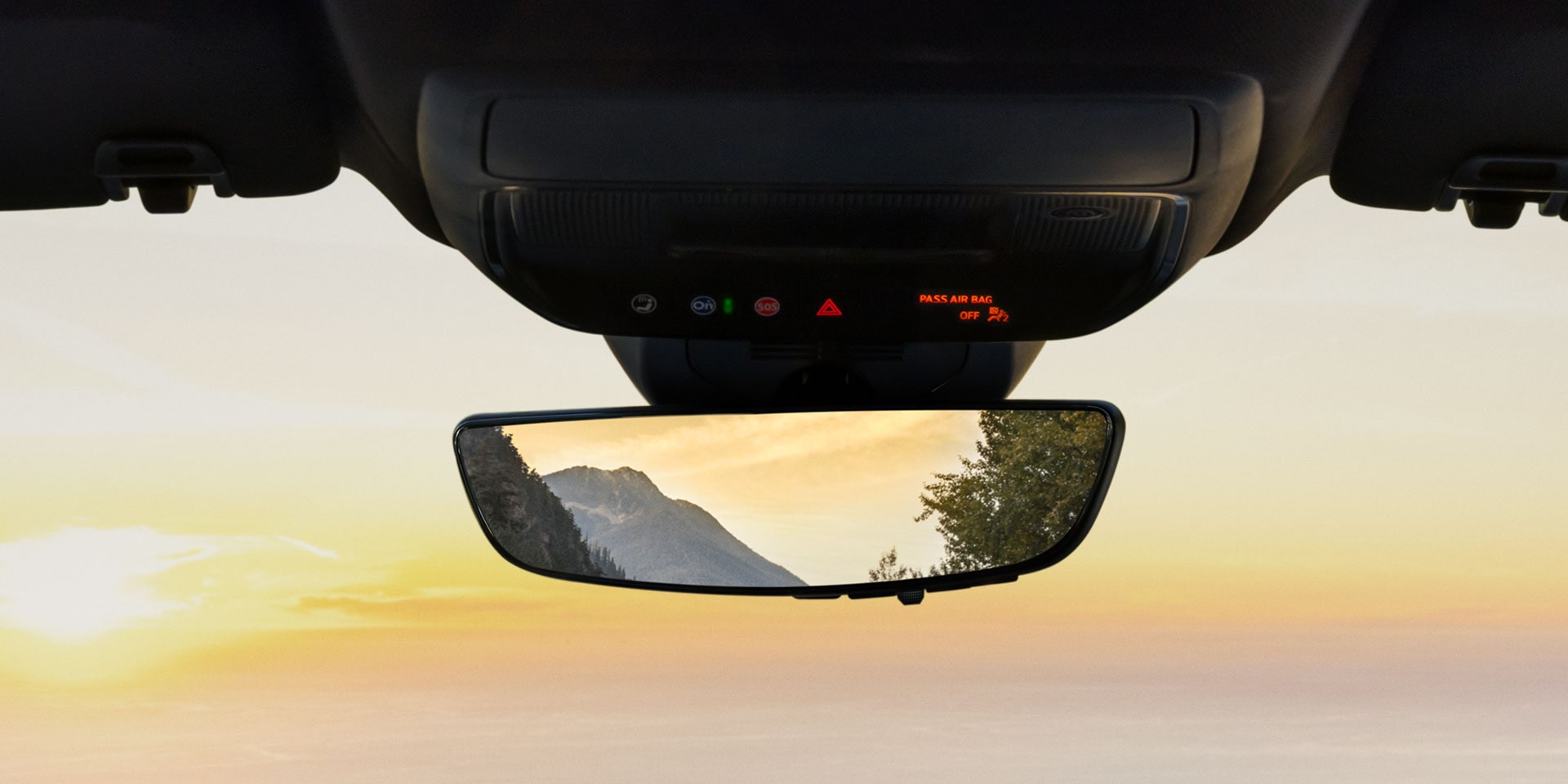 A Vehicle's Interior Overhead Console With 'PASS AIR BAG OFF' Displayed Above a Rear View Mirror Reflecting a Mountain and Water at Sunset
