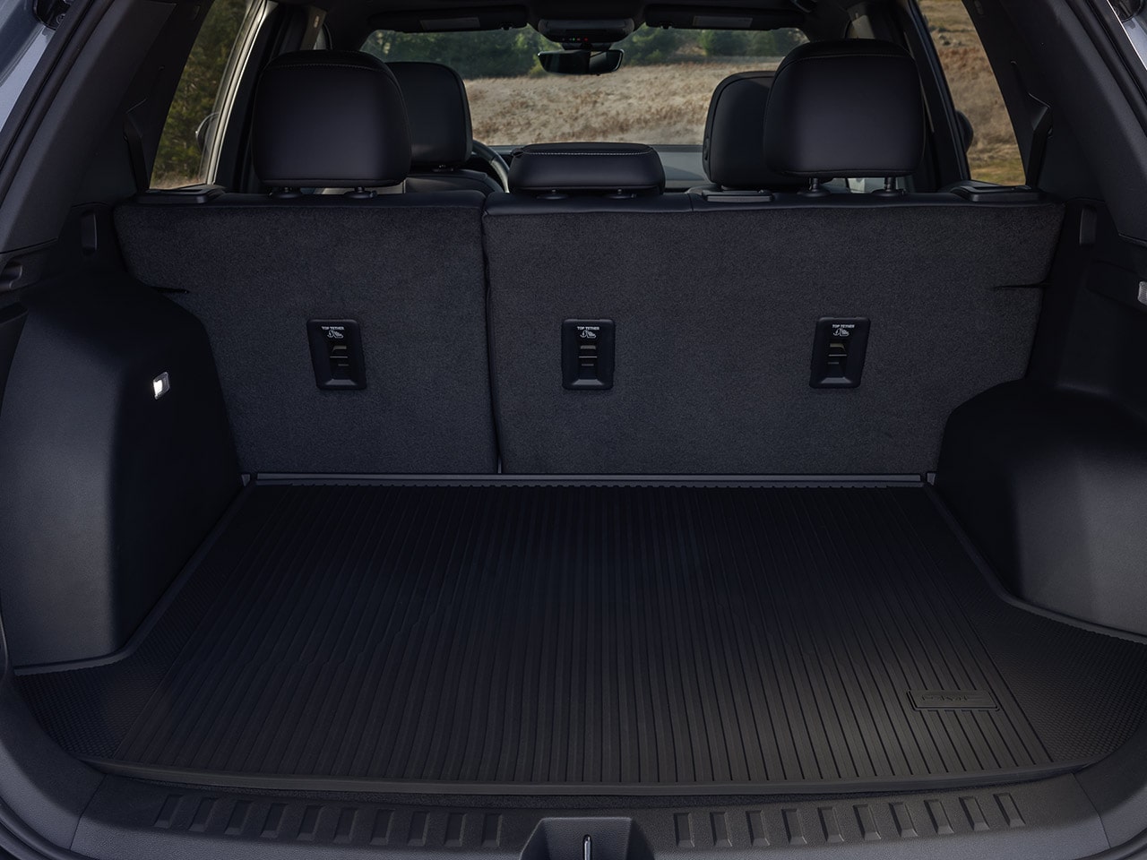 An Empty Black Trunk of a GMC Vehicle with Folded Up Rear Seats and a Ribbed Floor Liner