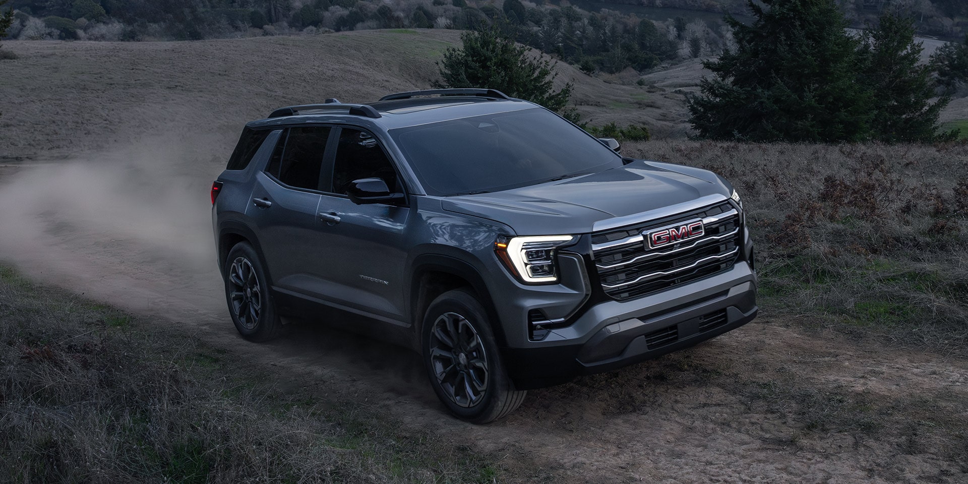 A Gray GMC Denali SUV Kicking Up Dust as it Drives on a Dirt Trail through a Valley