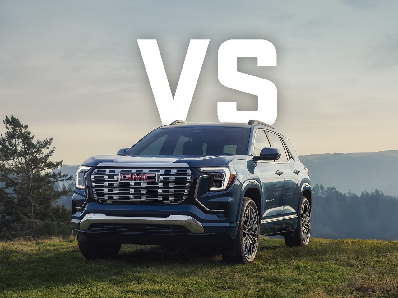 Front Three-quarters View of a Dark Blue GMC Terrain Parked on a Grassy Hillside with Large Bold Text Overlay Reading 'VS' Centered Above the SUV