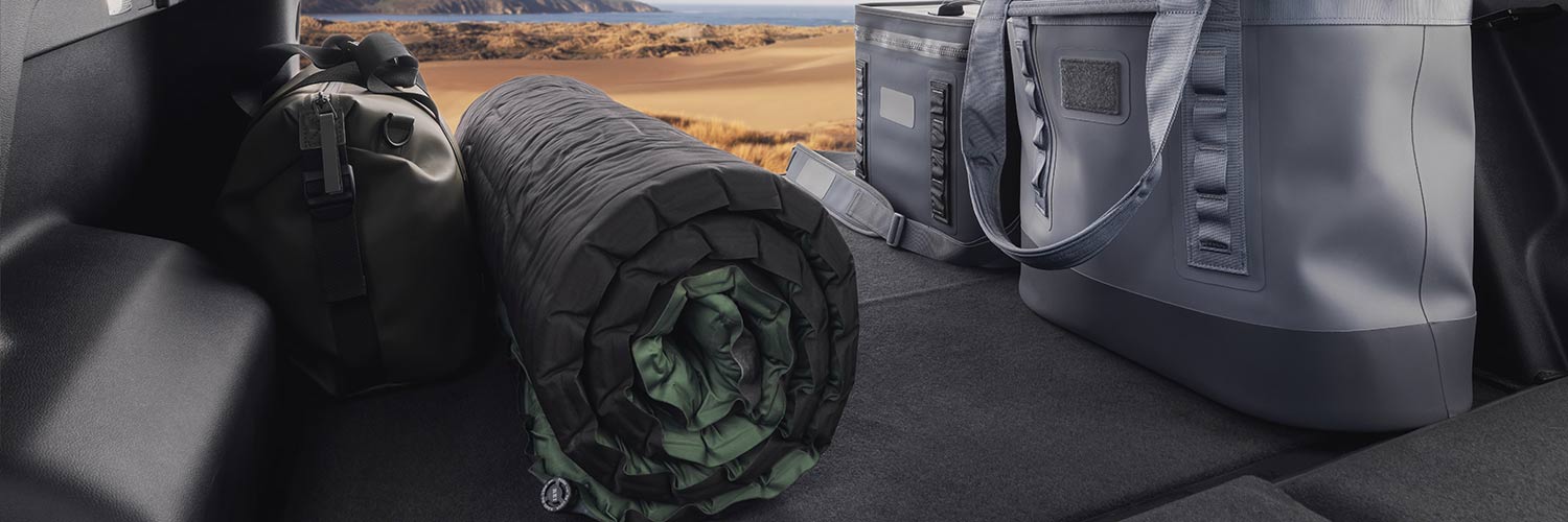 Camping Gear Including a Sleeping Mat and Cooler Bag in the Trunk of a GMC SUV with a Coastal Landscape Beyond