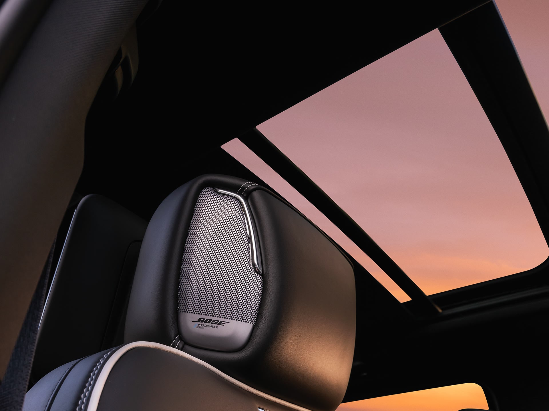 Rear Passenger View of the 2027 GMC Yukon Interior with a Panoramic Sunroof and Bose Speaker on the Headrest