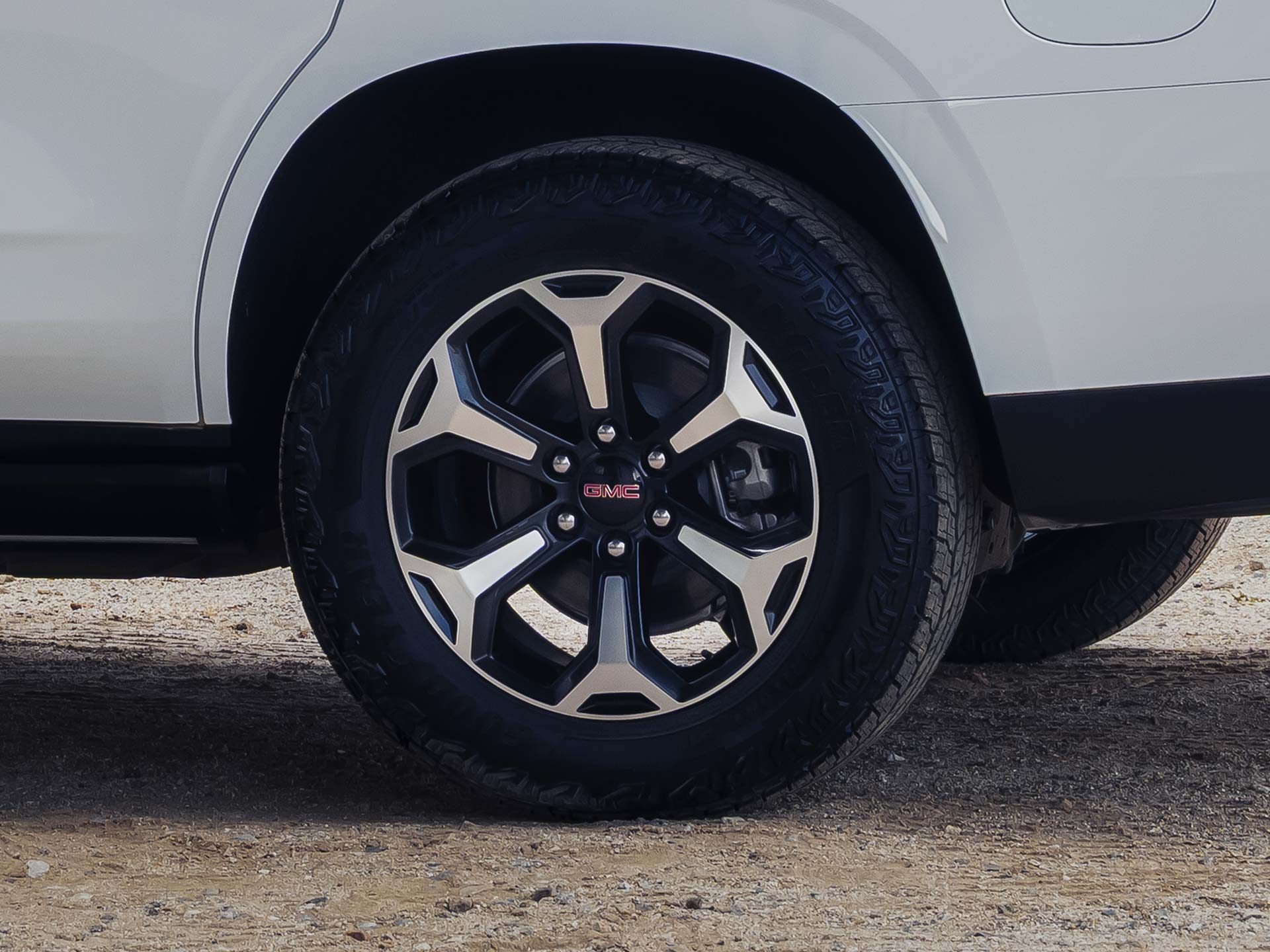 Close-up of the 2027 GMC Yukon Wheel with a Two-tone Multi-spoke Design on a Dirt Road