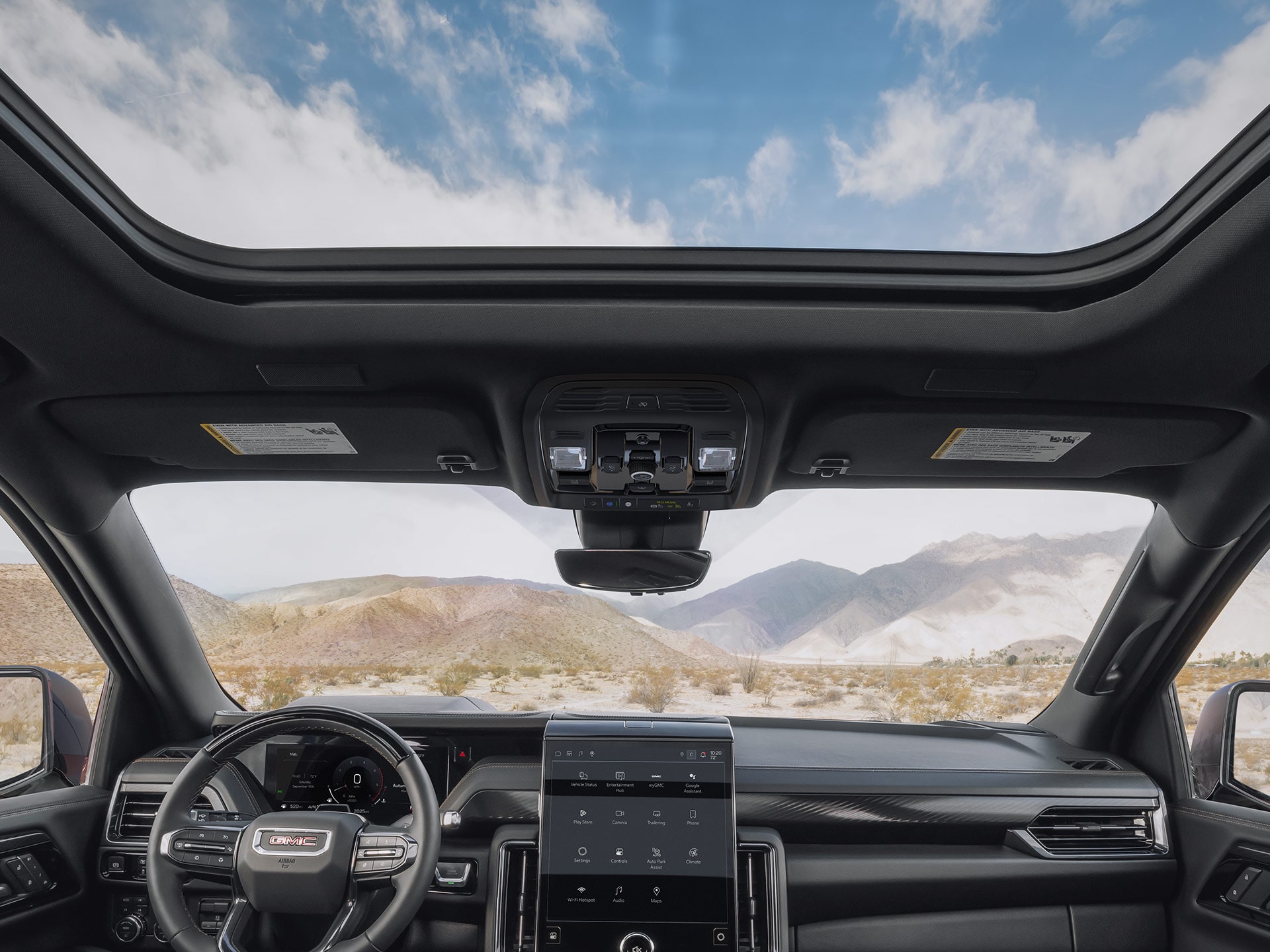 Interior Front Cabin View of the 2027 GMC Yukon with a Panoramic Sunroof and a Desert Mountain Landscape Outside