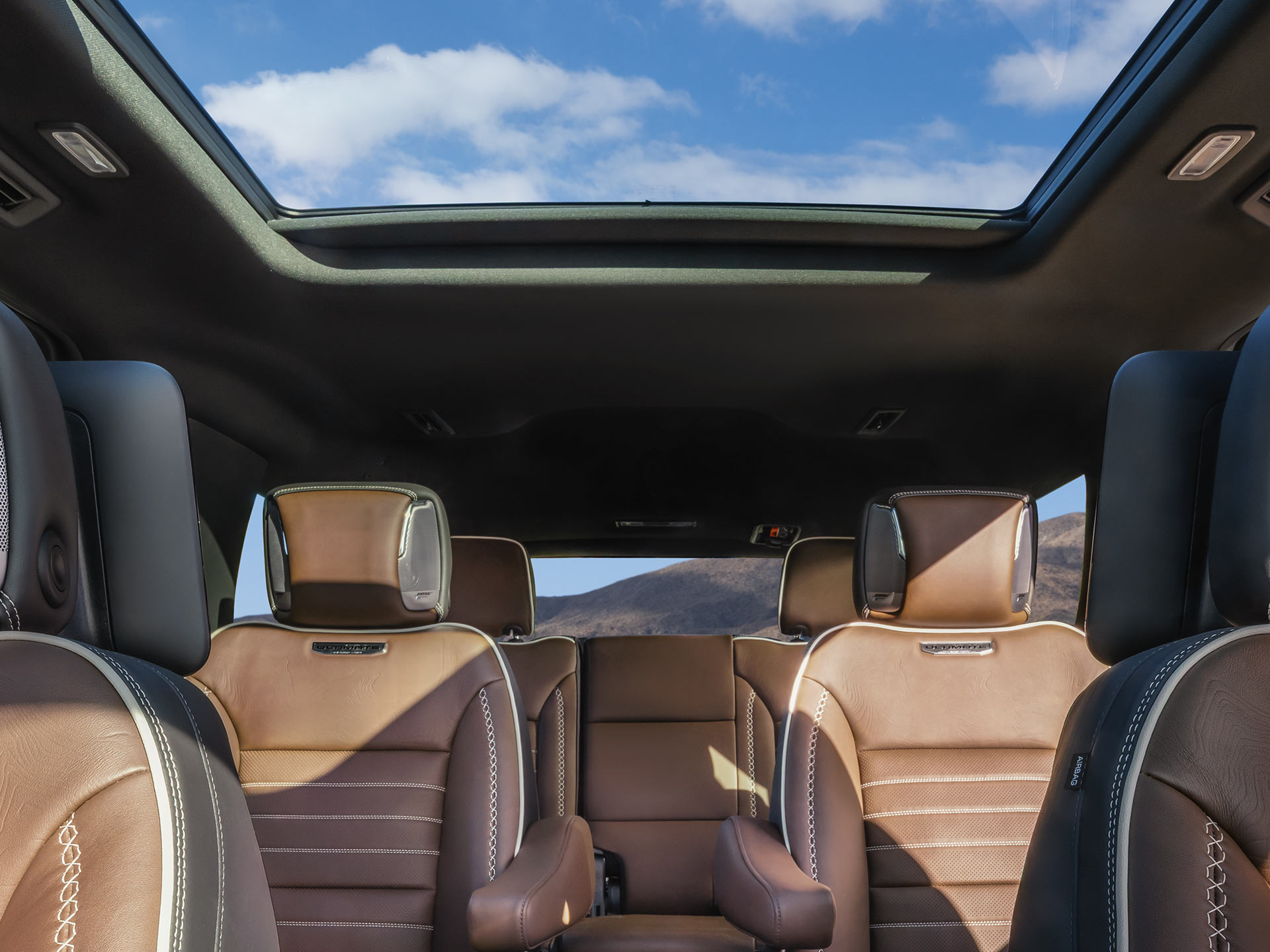 Rear Interior of a 2027 GMC Yukon Showcasing Brown Leather Seats and a Panoramic Sunroof with a Cloudy Sky Visible