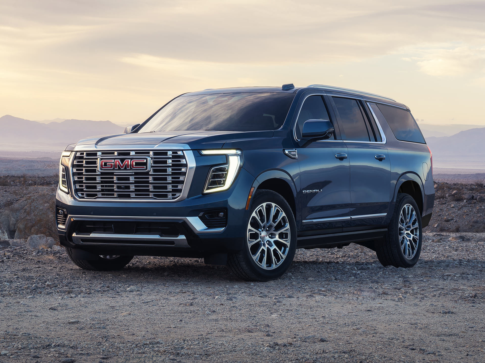 Three-Quarter Front View of a Dark Blue 2027 GMC Yukon Denali Parked on a Dirt Road in a Rocky, Mountainous Landscape