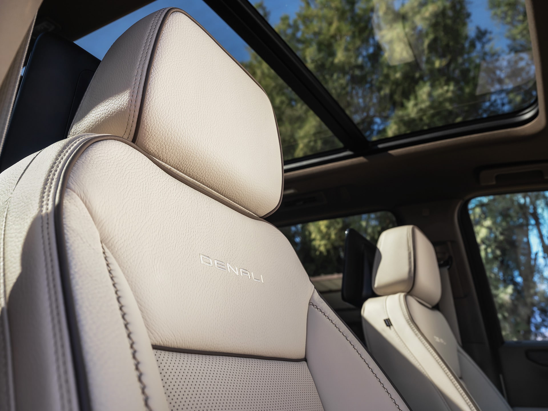 Close-Up of a Light-Colored Leather Seat with Denali Embossed, Underneath a Panoramic Sunroof Revealing Trees and Sky