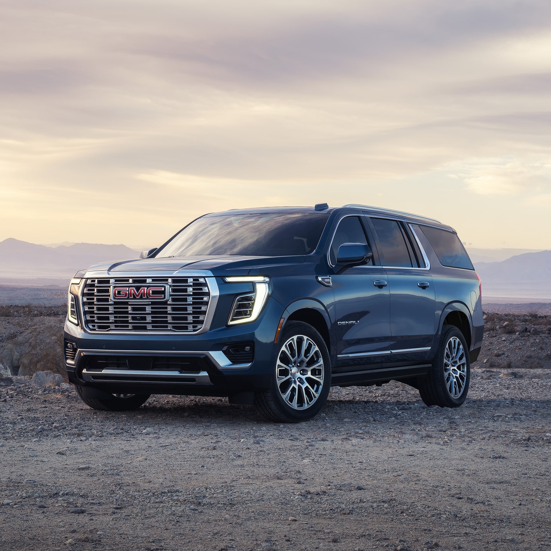 Three-Quarter Front View of a Dark Blue 2027 GMC Yukon Denali Parked on a Dirt Road in a Rocky, Mountainous Landscape