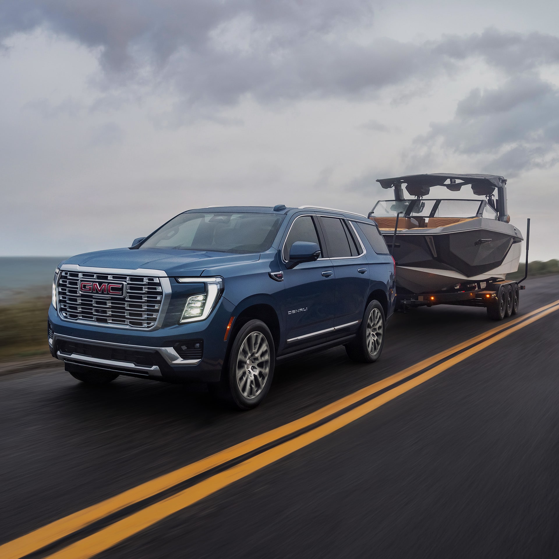 A Dark Blue 2027 GMC Yukon Towing a Boat on a Trailer on a Highway Next to the Ocean